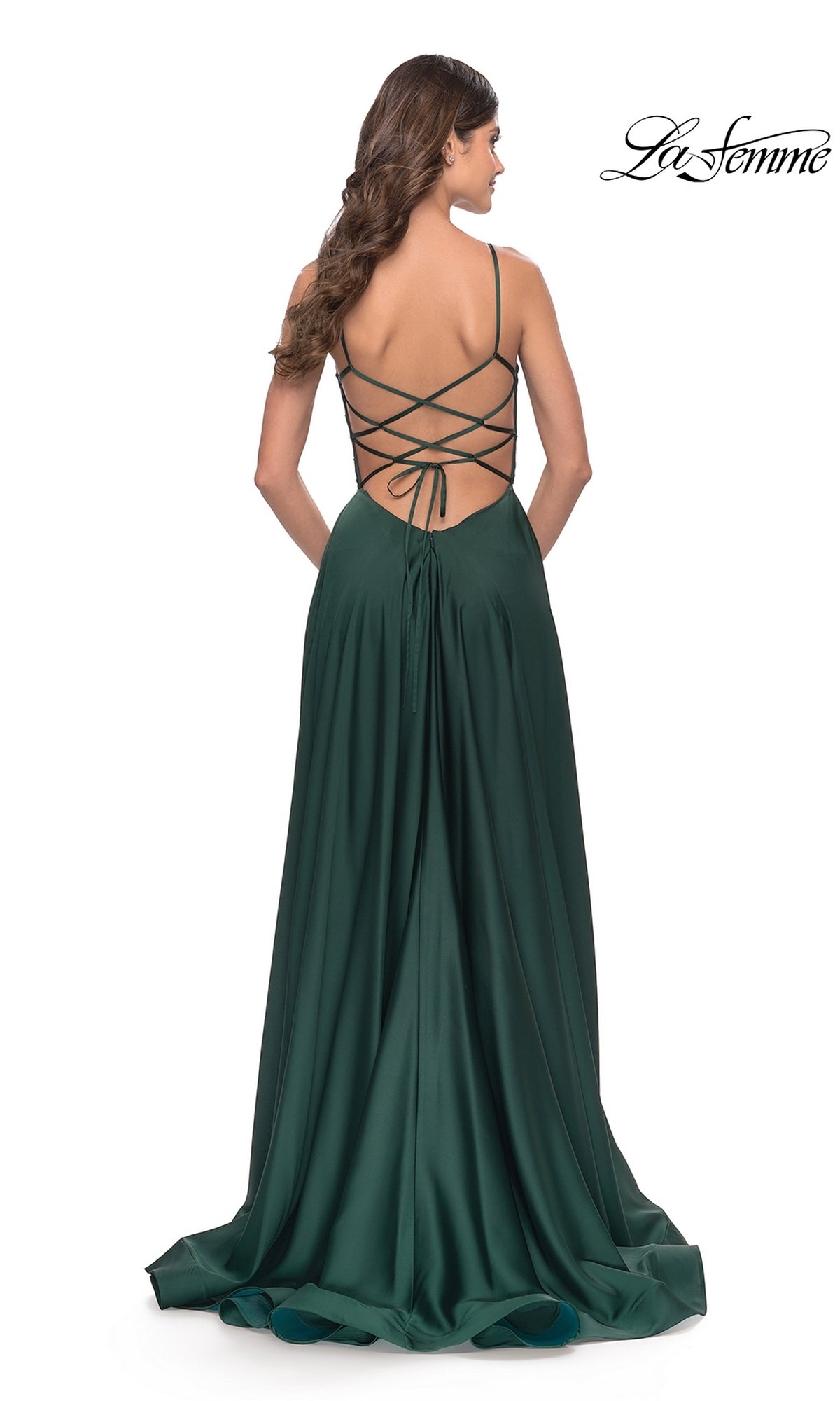 A woman stands facing away in the Corset-Back La Femme Long A-Line Prom Dress 31105, a dark green gown with thin straps, lace-up corset back, and a flowing floor-length skirt.